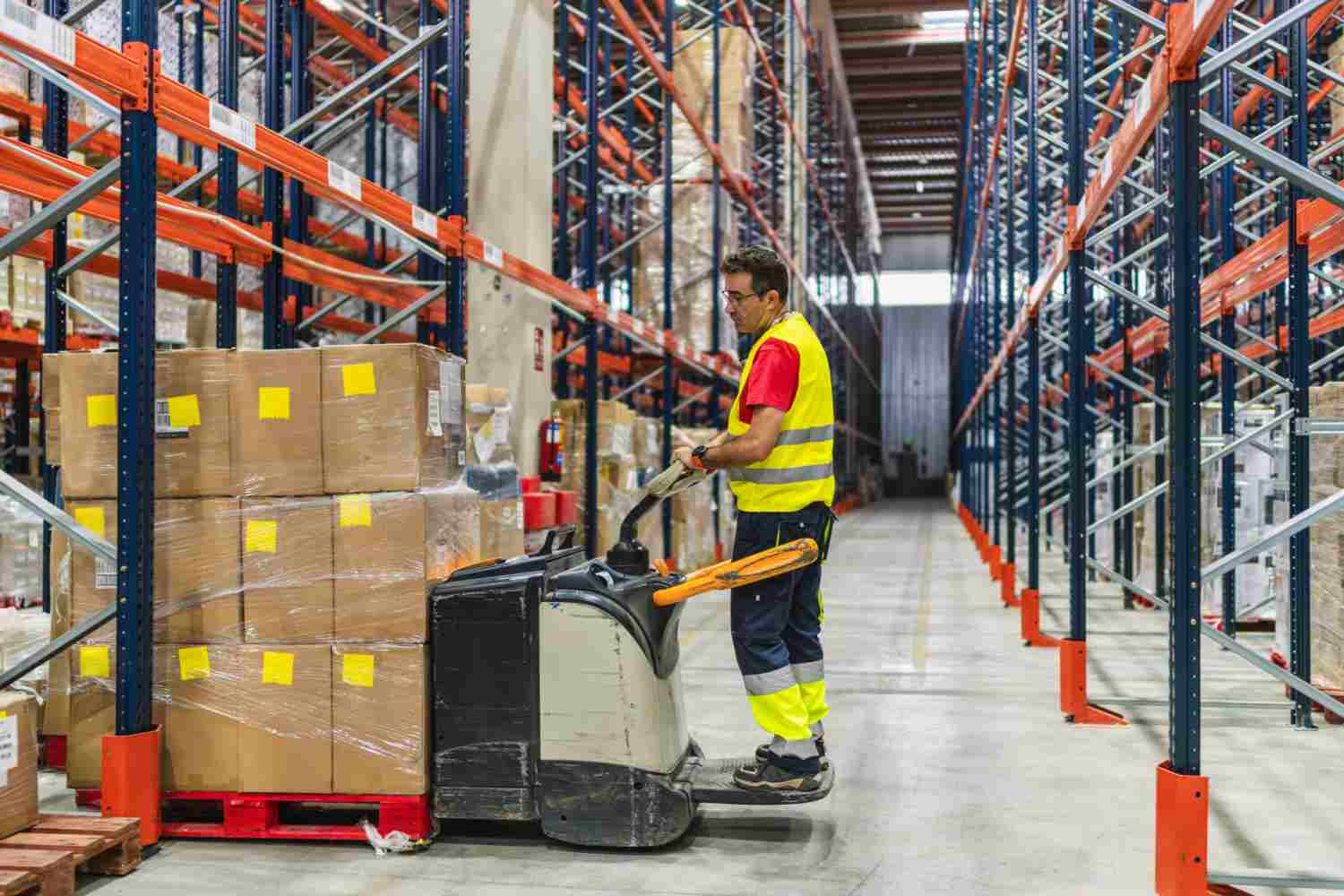Interior of storage warehouse, Worker with electric forklift pallet jack unloading pallet goods