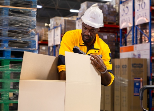 Male Warehouse worker packing boxes and filling them with products in a vest and hard hat